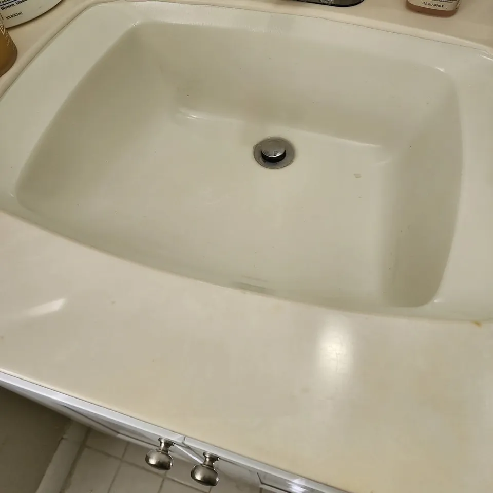 The same bathroom sink after cleaning, bright white basin and clean drain